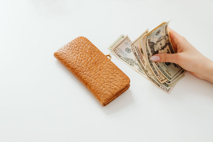 Hand holding US dollar bills beside a leather wallet, cash back vs discount codes for Shopify brands