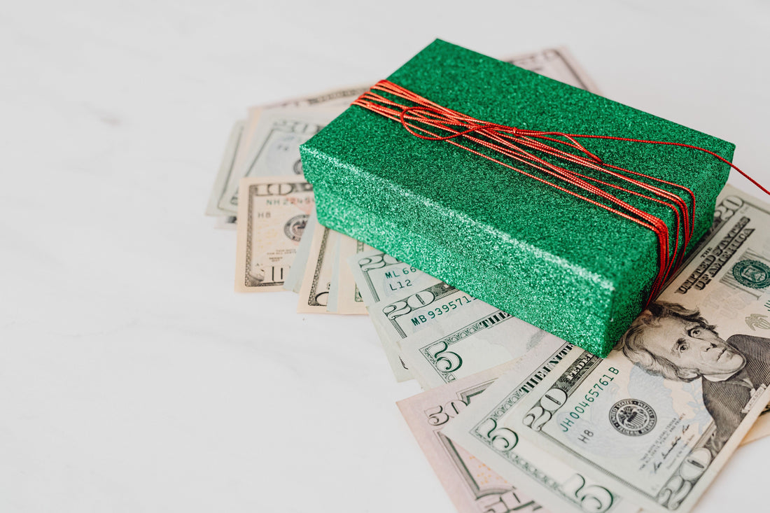 Green glitter gift box tied with red string resting on a fan of US dollar bills, representing cash rebates versus gift-card rewards