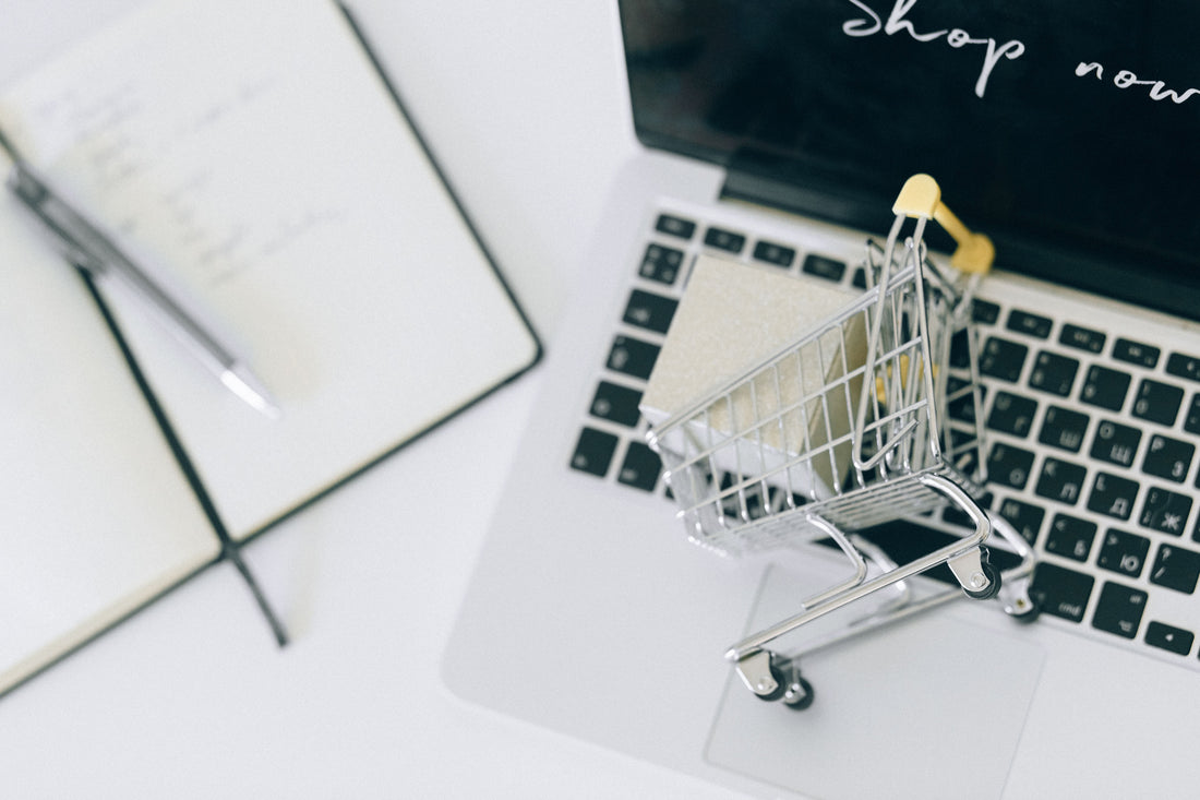 Mini shopping cart on a laptop keyboard next to a notebook, with “Shop now” on screen, for win-back campaigns