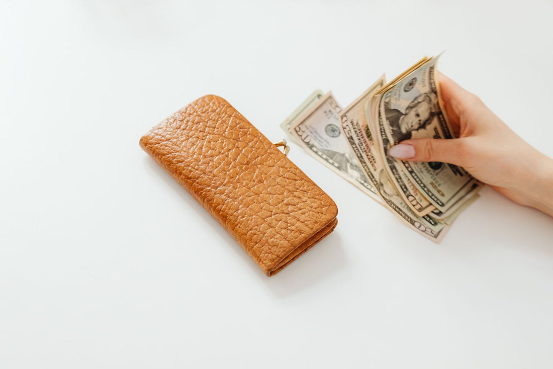 Hand holding US dollar bills beside a leather wallet, cash back vs discount codes for Shopify brands